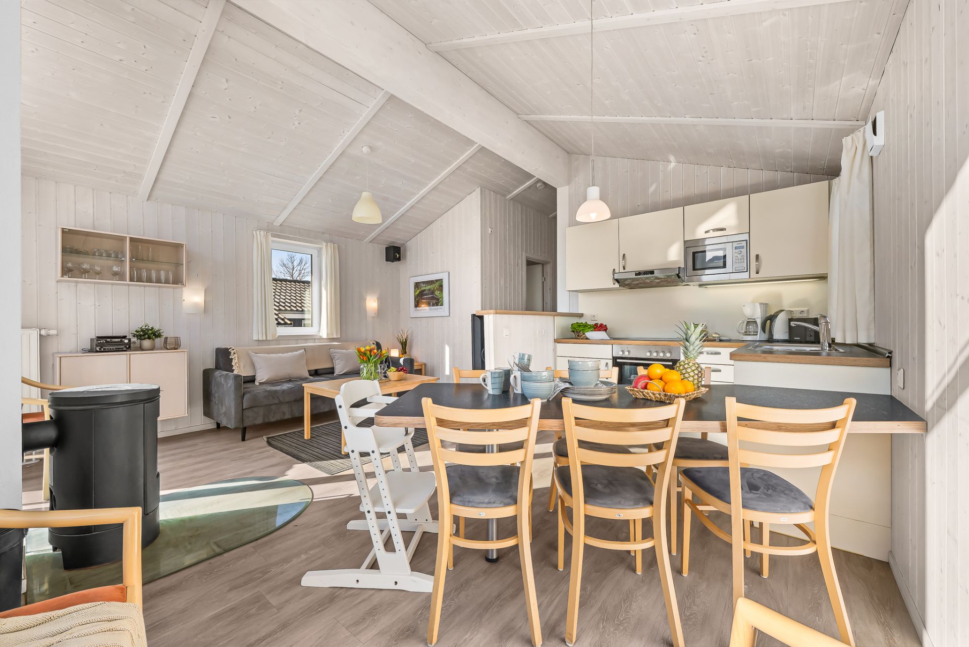 Helles Wohnzimmer mit offener Küche, Esstisch, Stühlen und Sofa.