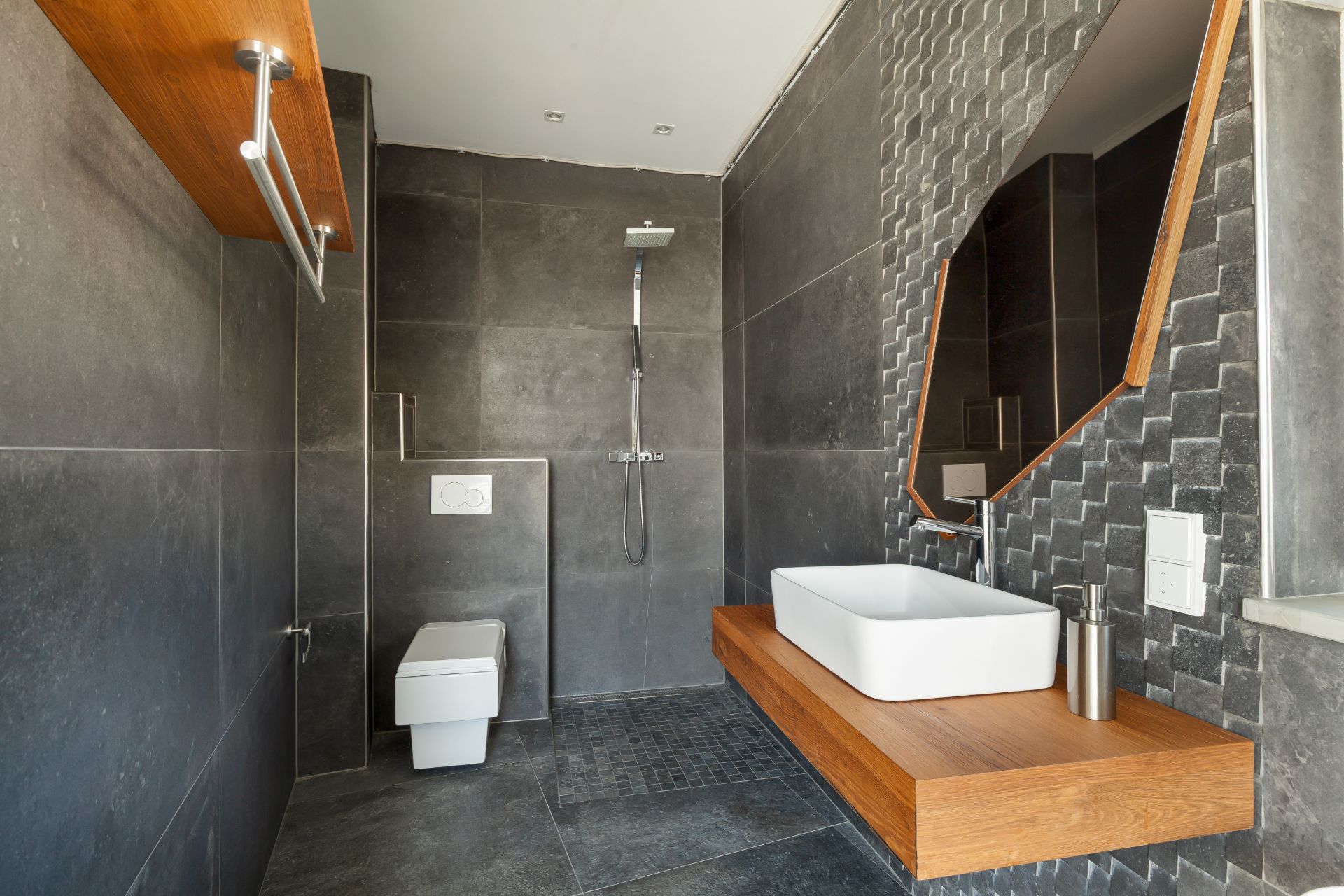Modernes Badezimmer mit grauen Fliesen, Dusche, WC, Holzwaschtisch und großem Spiegel.