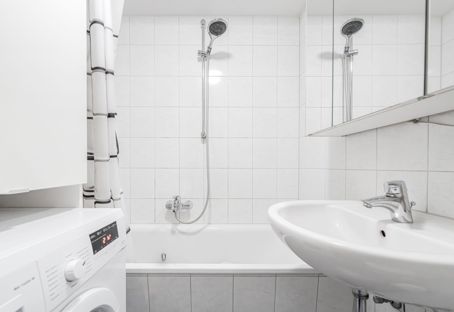 Kleines Badezimmer mit Badewanne, Waschbecken, Duschkopf und Waschmaschine.