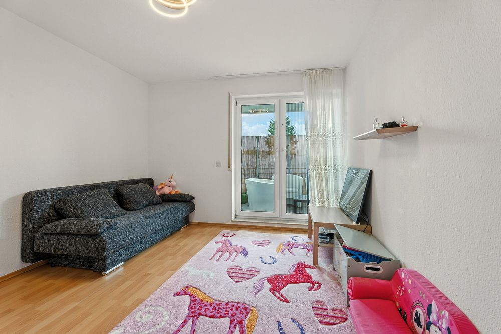 Wohnzimmer mit Sofa, Fernseher, Kinderspielzeug und buntem Teppich mit Pferdemotiven.