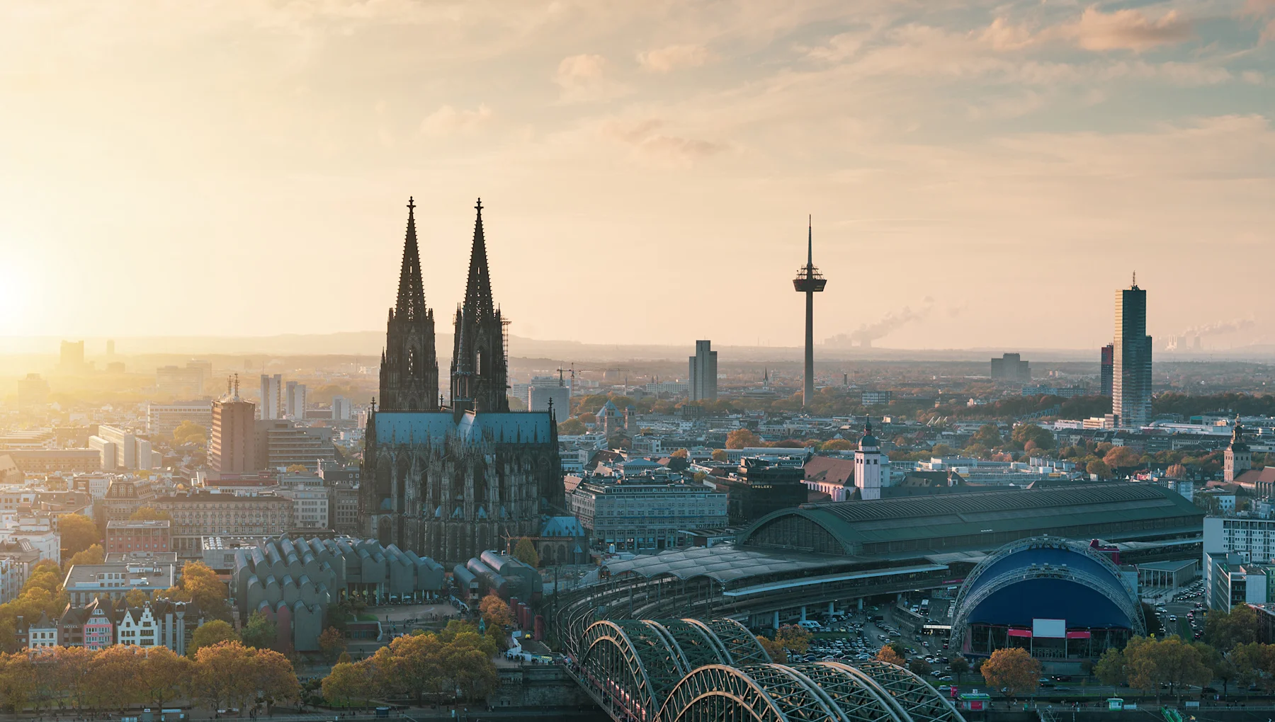 Stadtpanorama mit Kirche, Fernsehturm, Bahnhof und Brücke im Vordergrund bei Sonnenuntergang.