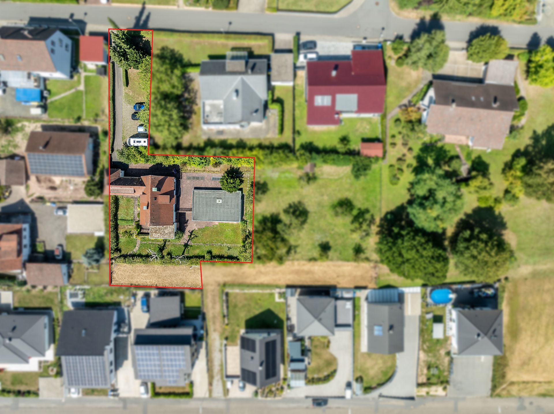 Luftaufnahme eines Hauses mit Grundstück, von roter Linie umrandet, umgeben von weiteren Wohnhäusern.
