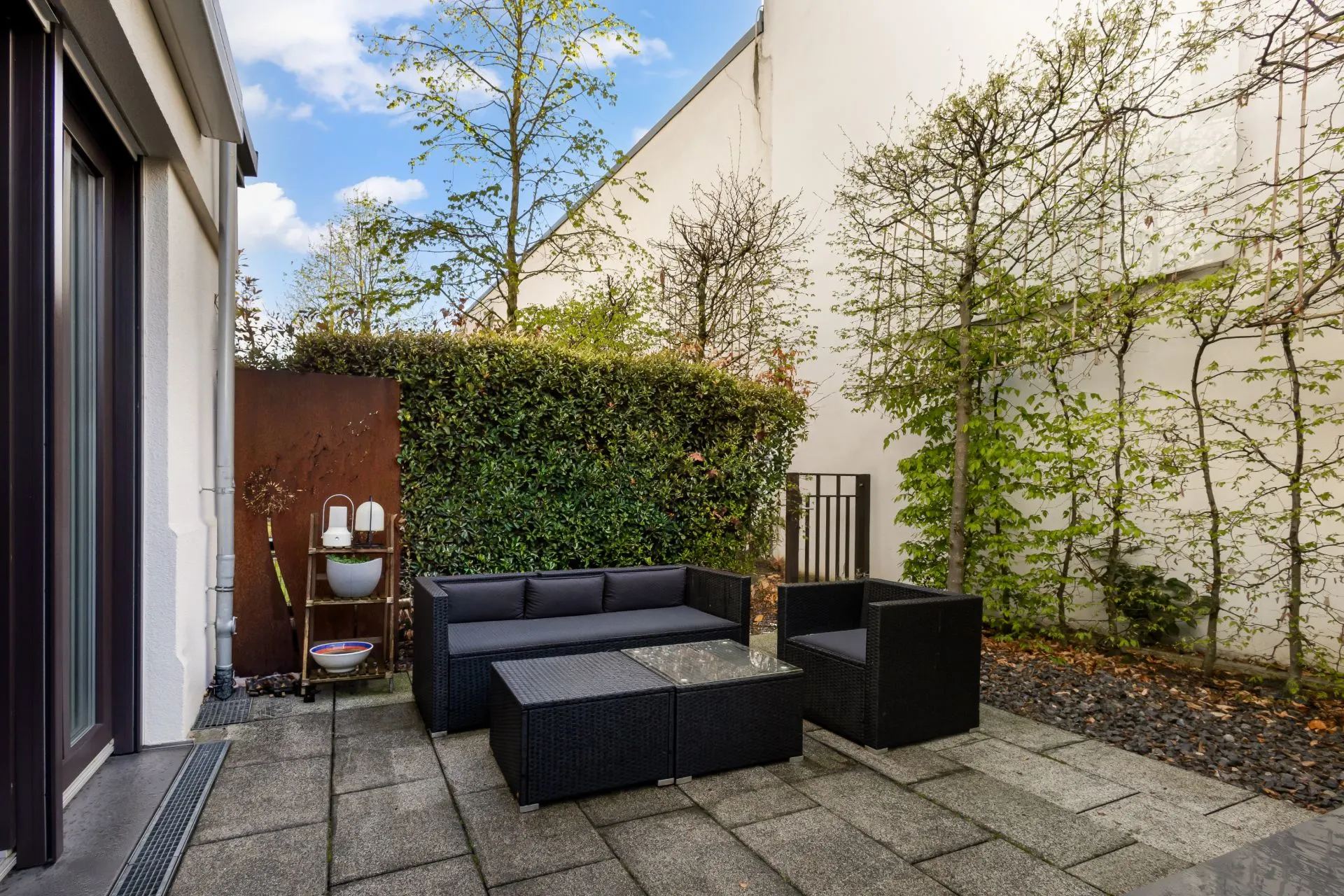Moderne Terrasse mit Sitzgruppe, Pflanzenwand und Fliesenboden in einem Innenhof.