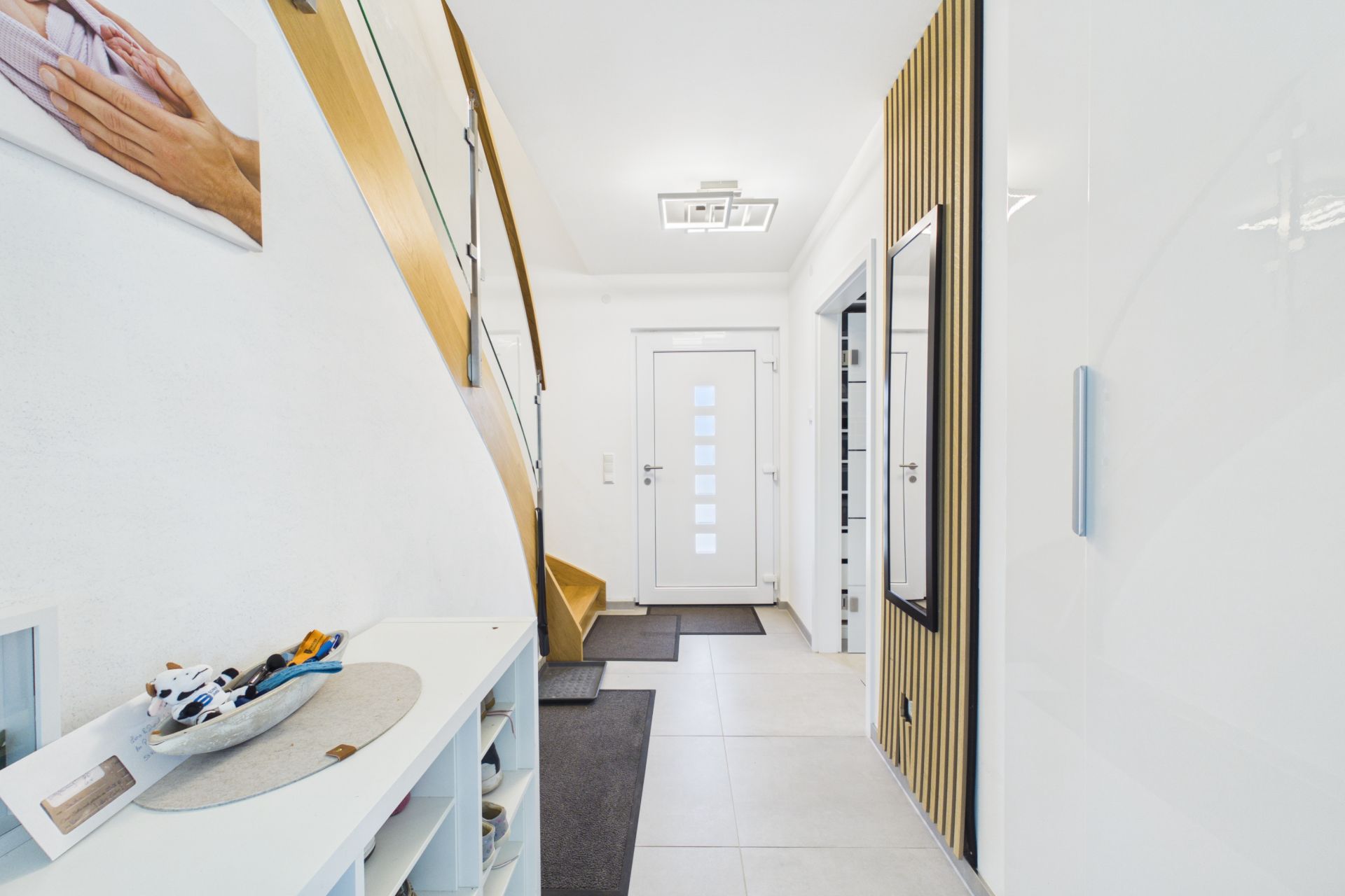 Heller Flur mit weißer Eingangstür, Treppe, Spiegel und Regal mit Spielsachen.