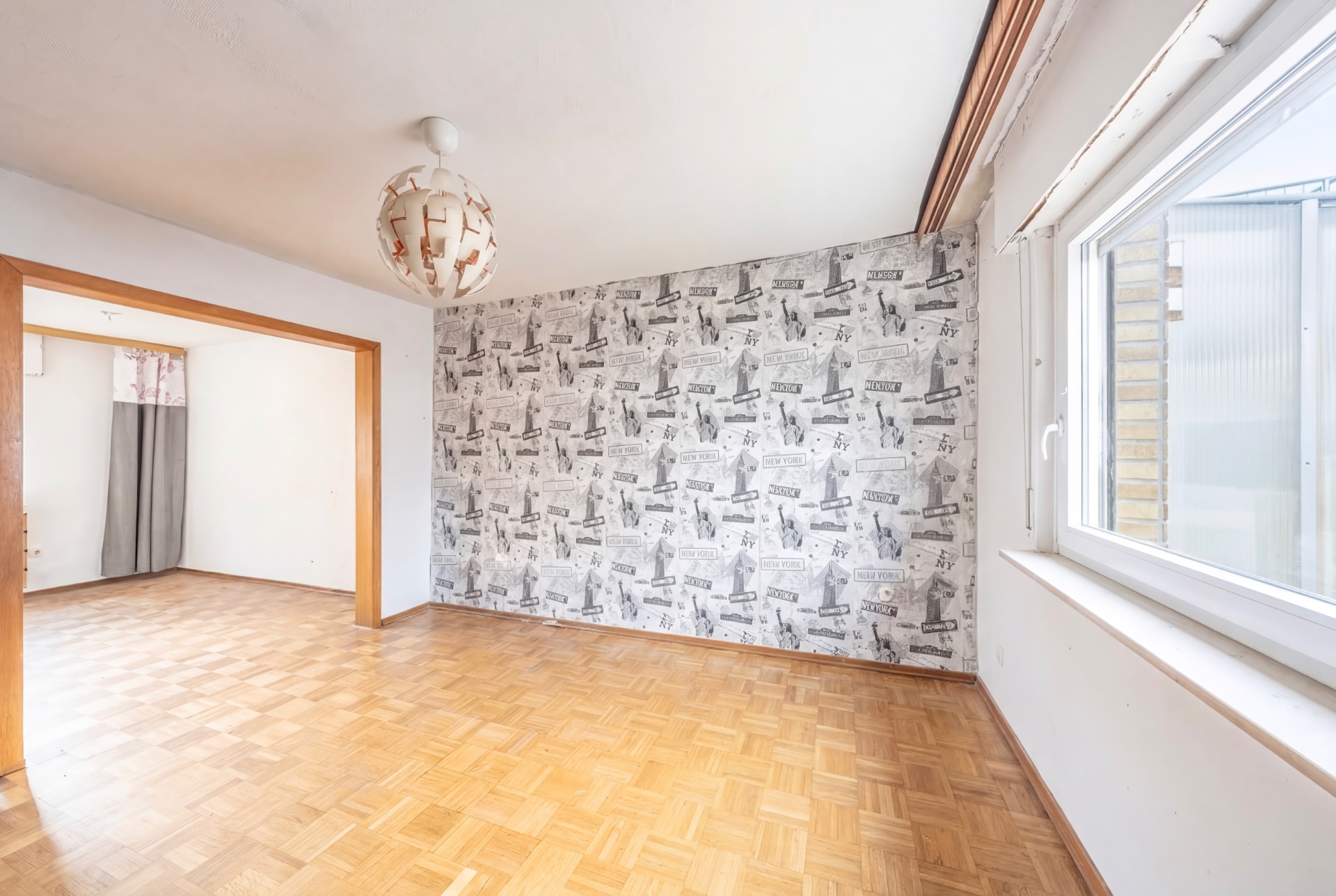 Helles Zimmer mit Parkettboden, Tapetenwand mit Muster und großem Fenster.