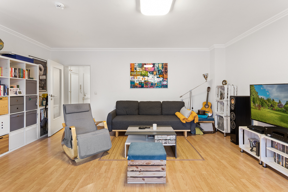 Modernes Wohnzimmer mit grauem Sofa, Sessel, TV, Regalwand und Holzfußboden.