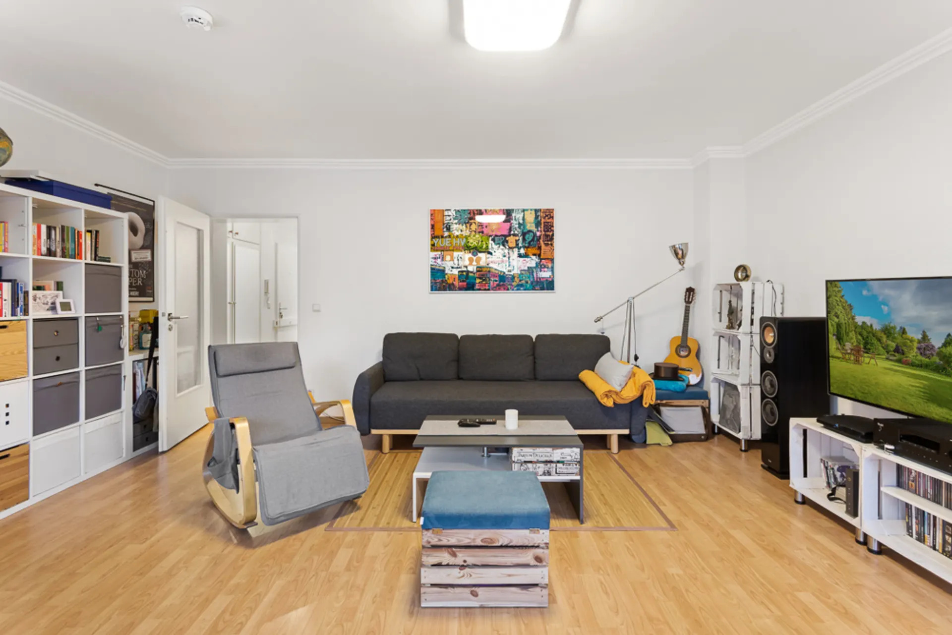 Modernes Wohnzimmer mit grauem Sofa, Sessel, TV, Regalwand und Holzfußboden.