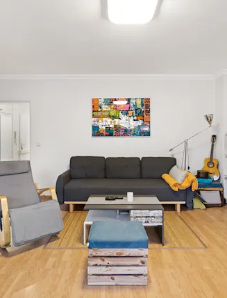 Modernes Wohnzimmer mit grauem Sofa, Sessel, TV, Regalwand und Holzfußboden.