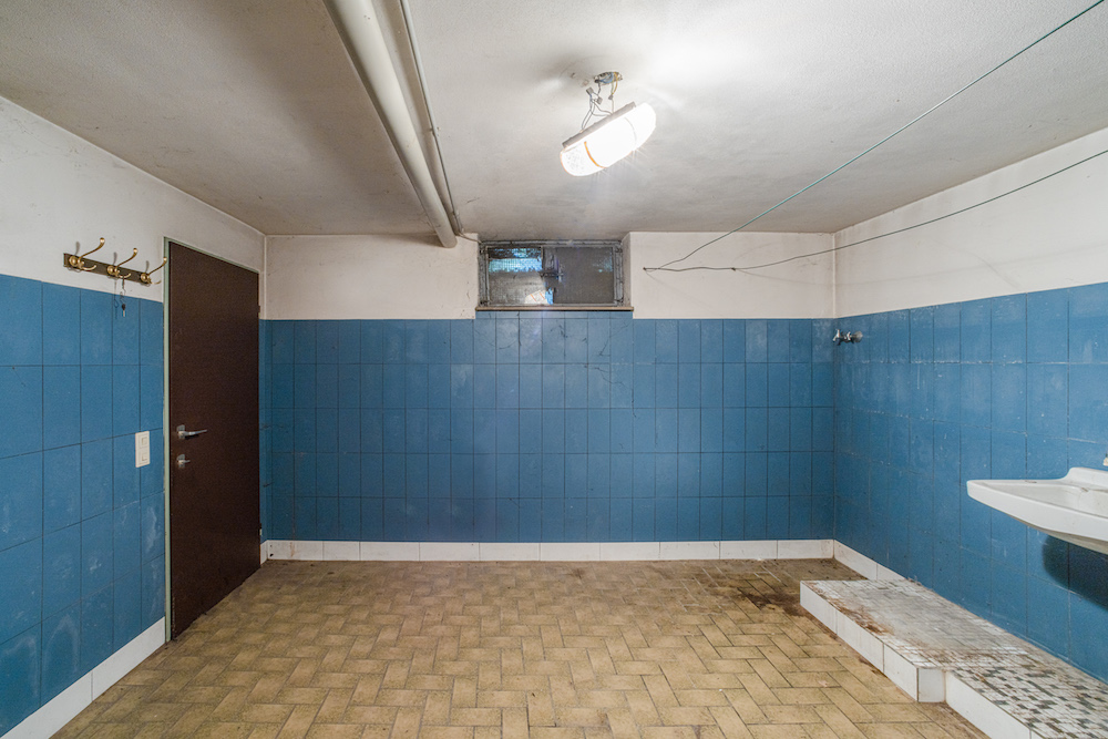 Kellerraum mit blauen Fliesen, brauner Tür, Waschbecken und Haken an der Wand.