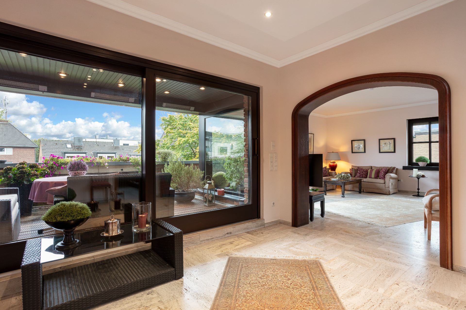 Helles Wohnzimmer mit Zugang zur überdachten Terrasse, die mit Pflanzen und Möbeln dekoriert ist.