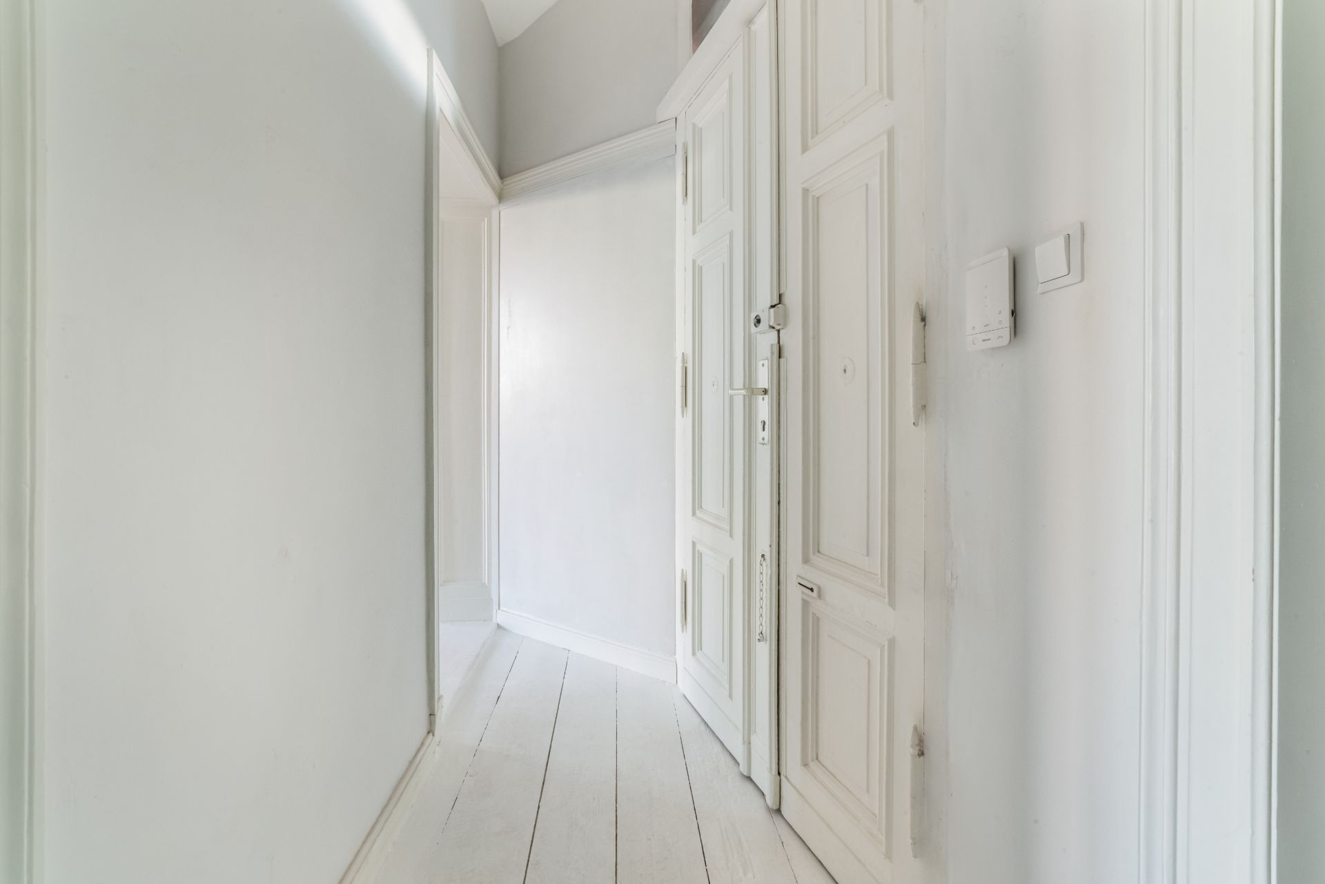 Heller Flur mit weißen Wänden, Holzboden und großer Holztür.