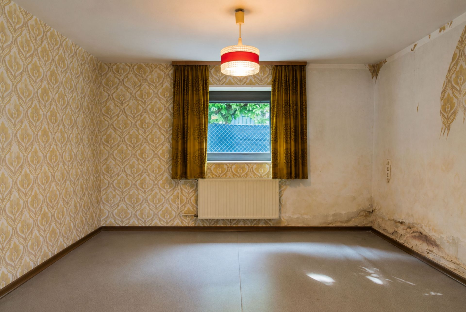 Leerer Raum mit Tapeten, Fenster, braunen Vorhängen und Wasserschäden an der Wand.