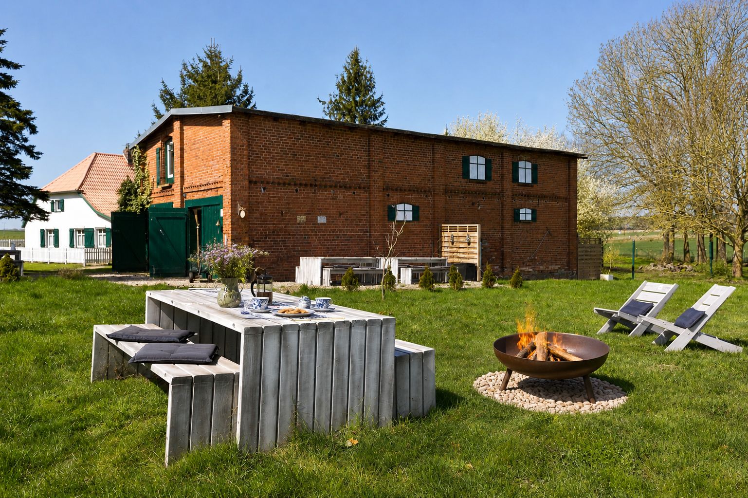 Garten mit Feuerschale, Holztisch und Liegestühlen vor einem Backsteinhaus.