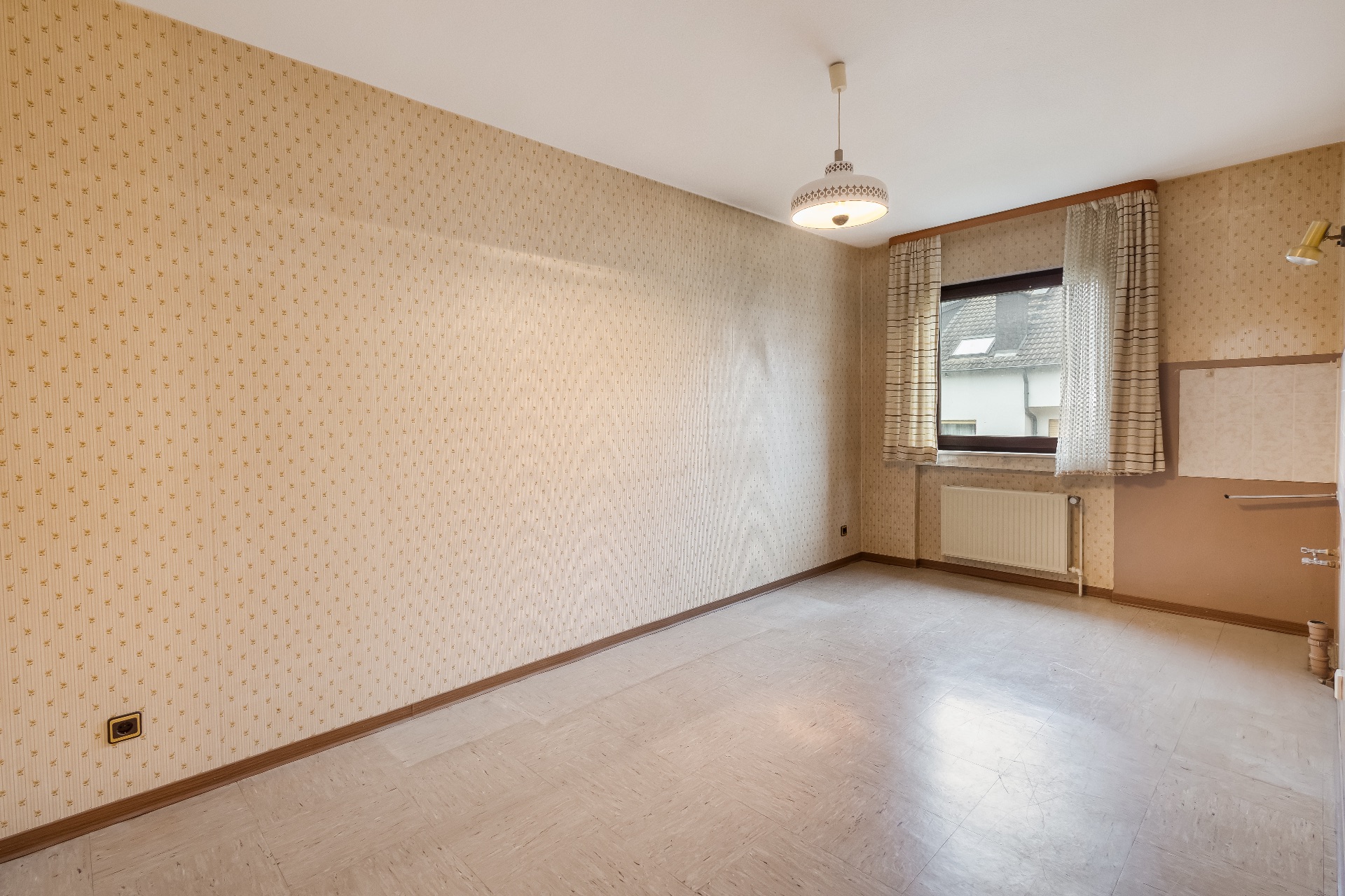 Leeres Zimmer mit gemusterten Tapeten, Fenster mit Gardinen und Deckenleuchte.