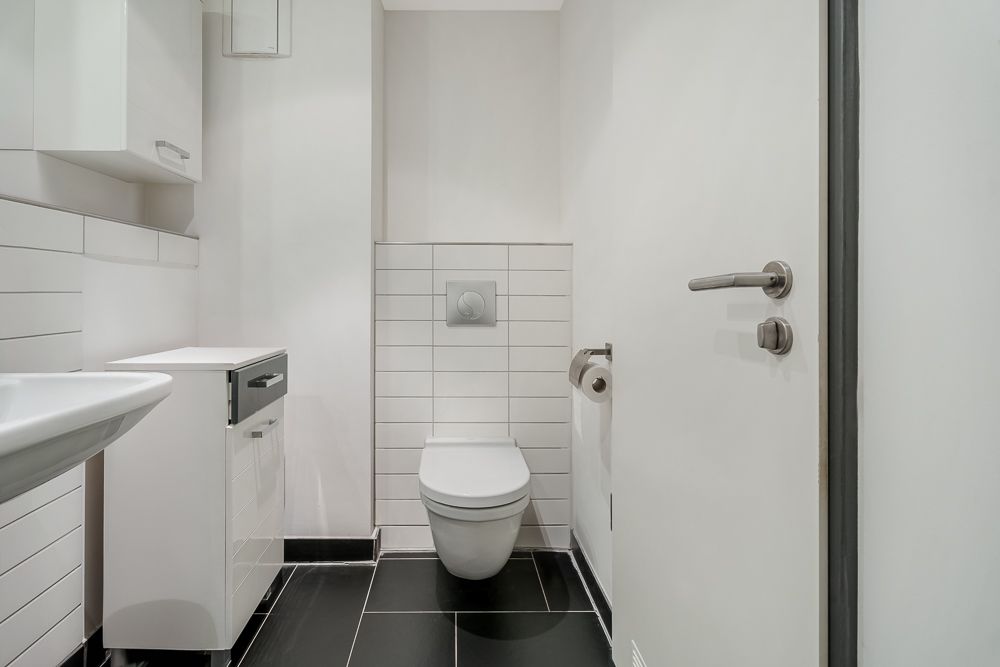 Modernes Badezimmer mit wandhängender Toilette, Waschbecken und weißen Fliesen.