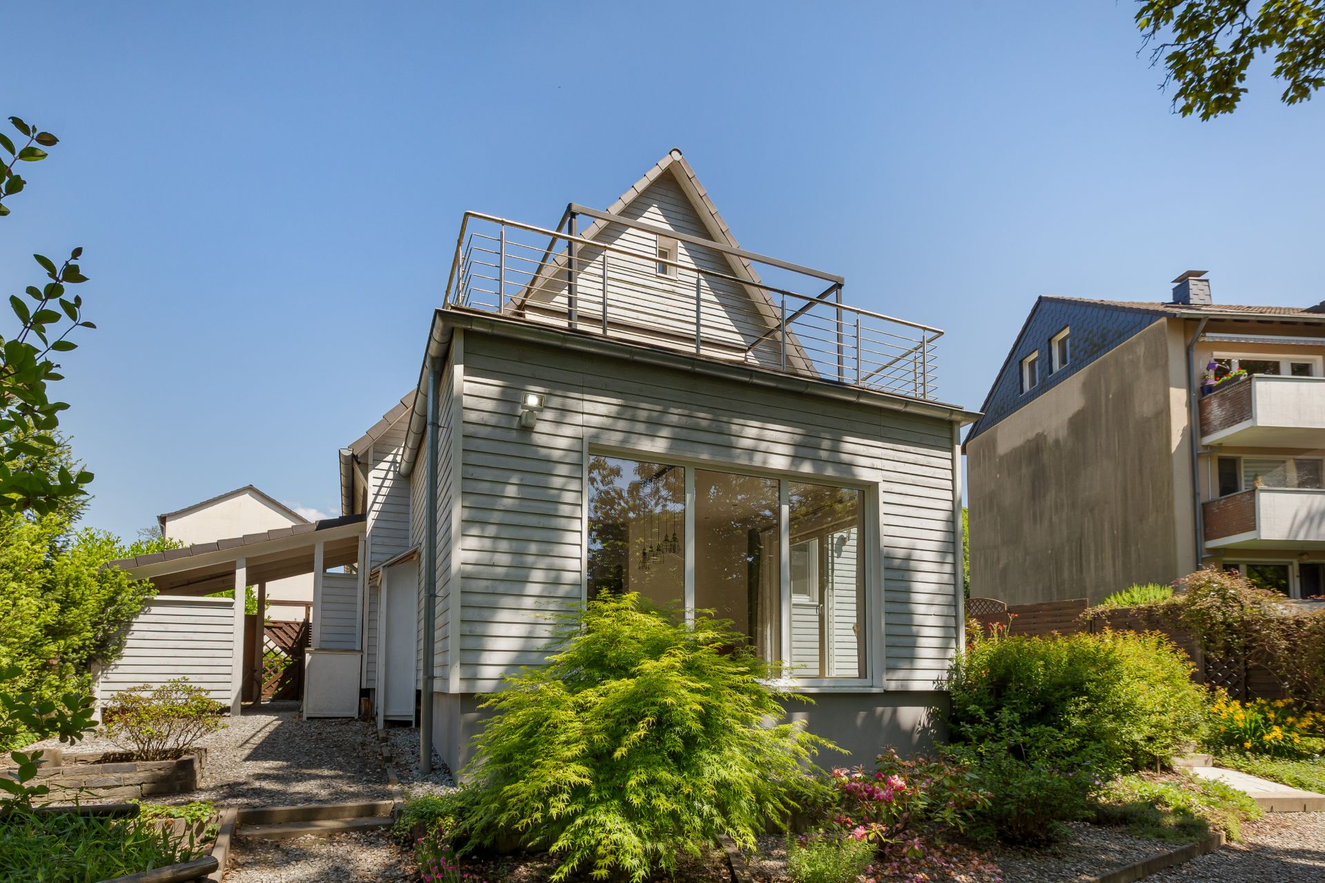 Modernes weißes Einfamilienhaus mit großem Fenster und Garten, sonniges Wetter.