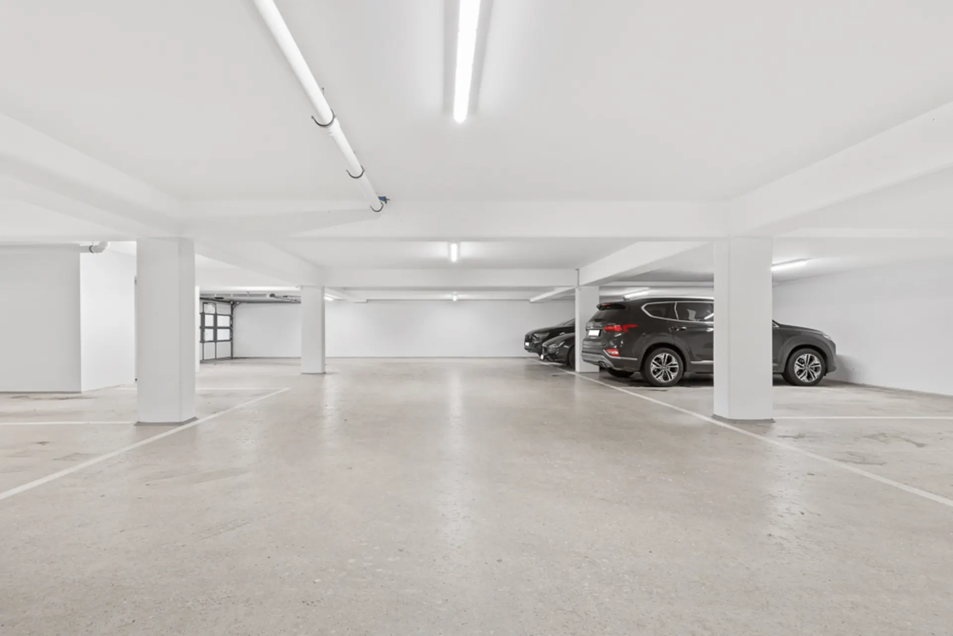 Helle, saubere Tiefgarage mit mehreren geparkten Autos und freien Parkplätzen.