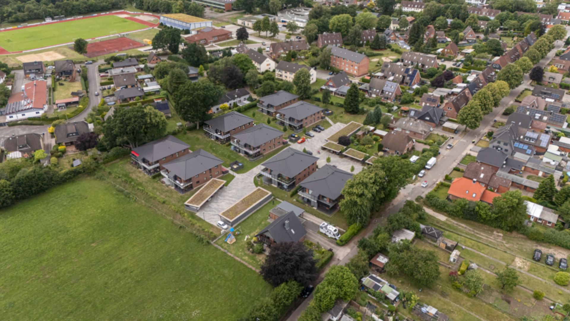 Luftaufnahme eines Wohngebiets mit mehreren Häusern, Straßen und viel Grünfläche.