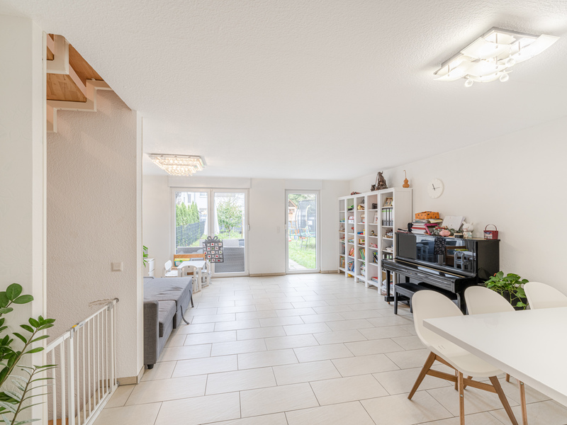 Helles Wohnzimmer mit Klavier, Bücherregalen, Esstisch und Zugang zum Garten.