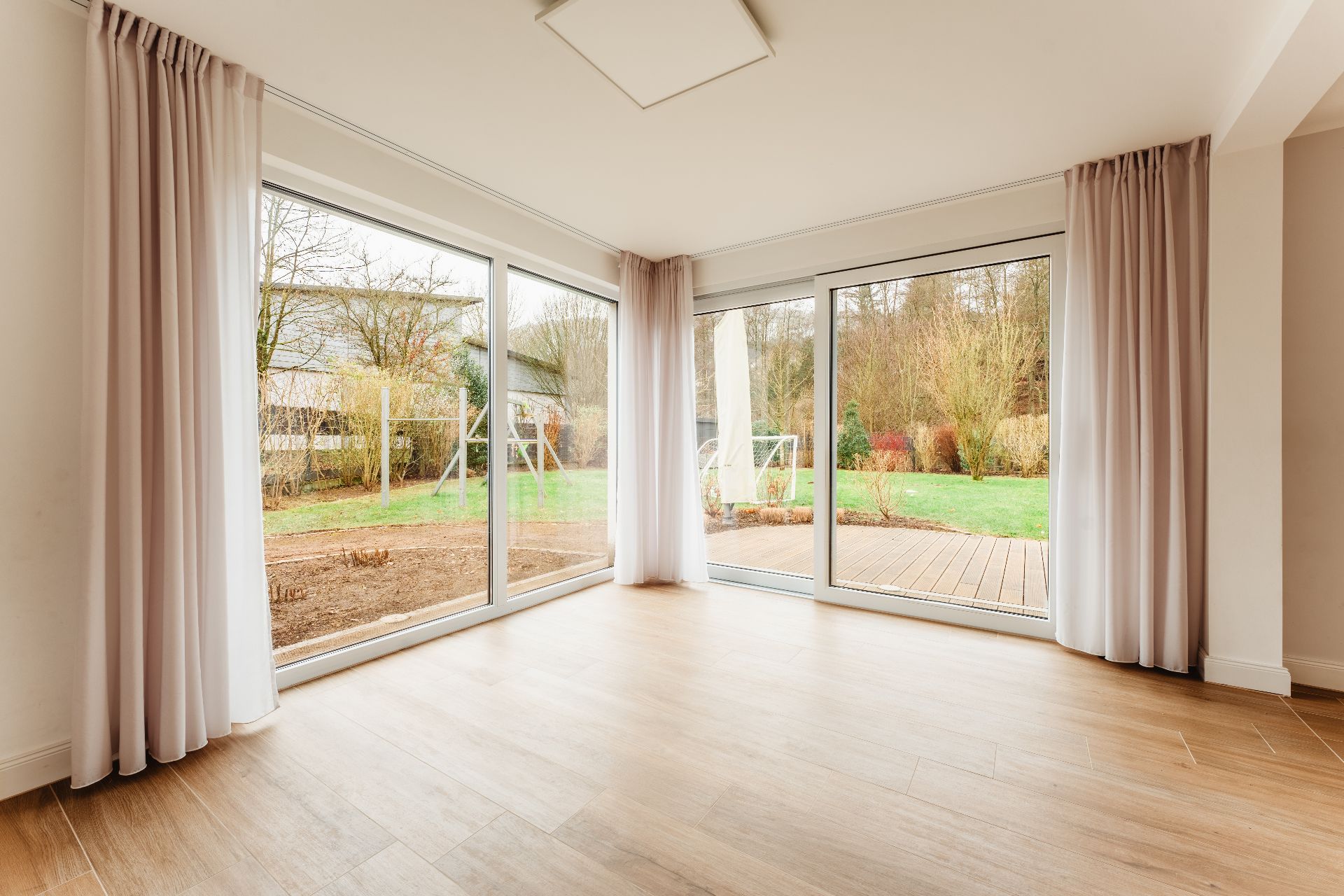 Helles Wohnzimmer mit großen Fensterfronten, Vorhängen und Blick auf den Garten.
