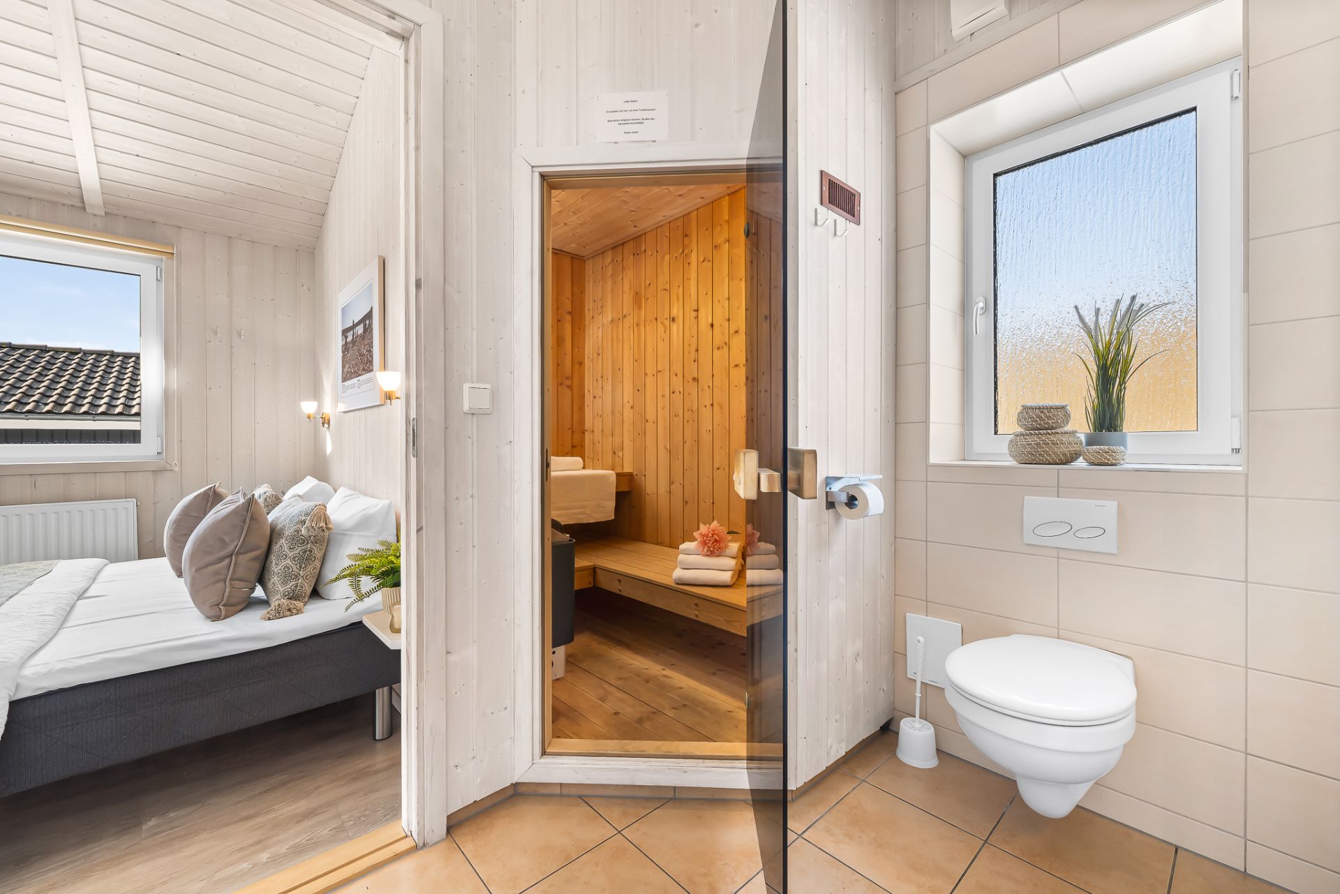 Modernes Badezimmer mit Sauna, WC, Fenster und Blick ins angrenzende Schlafzimmer.