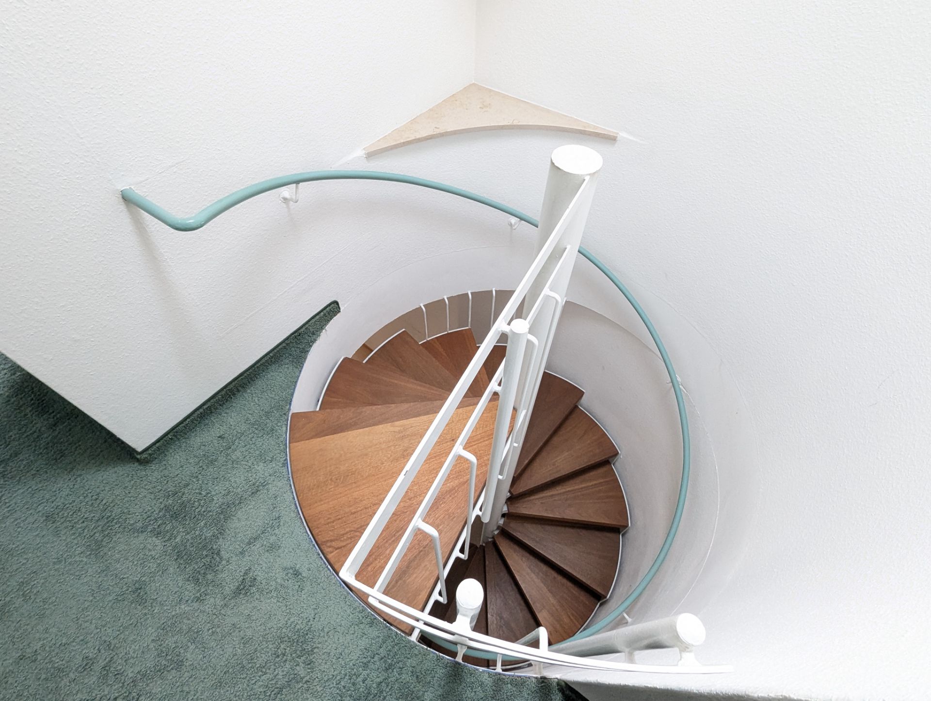 Holz-Wendeltreppe mit weißem Geländer und grünem Teppichboden oben.