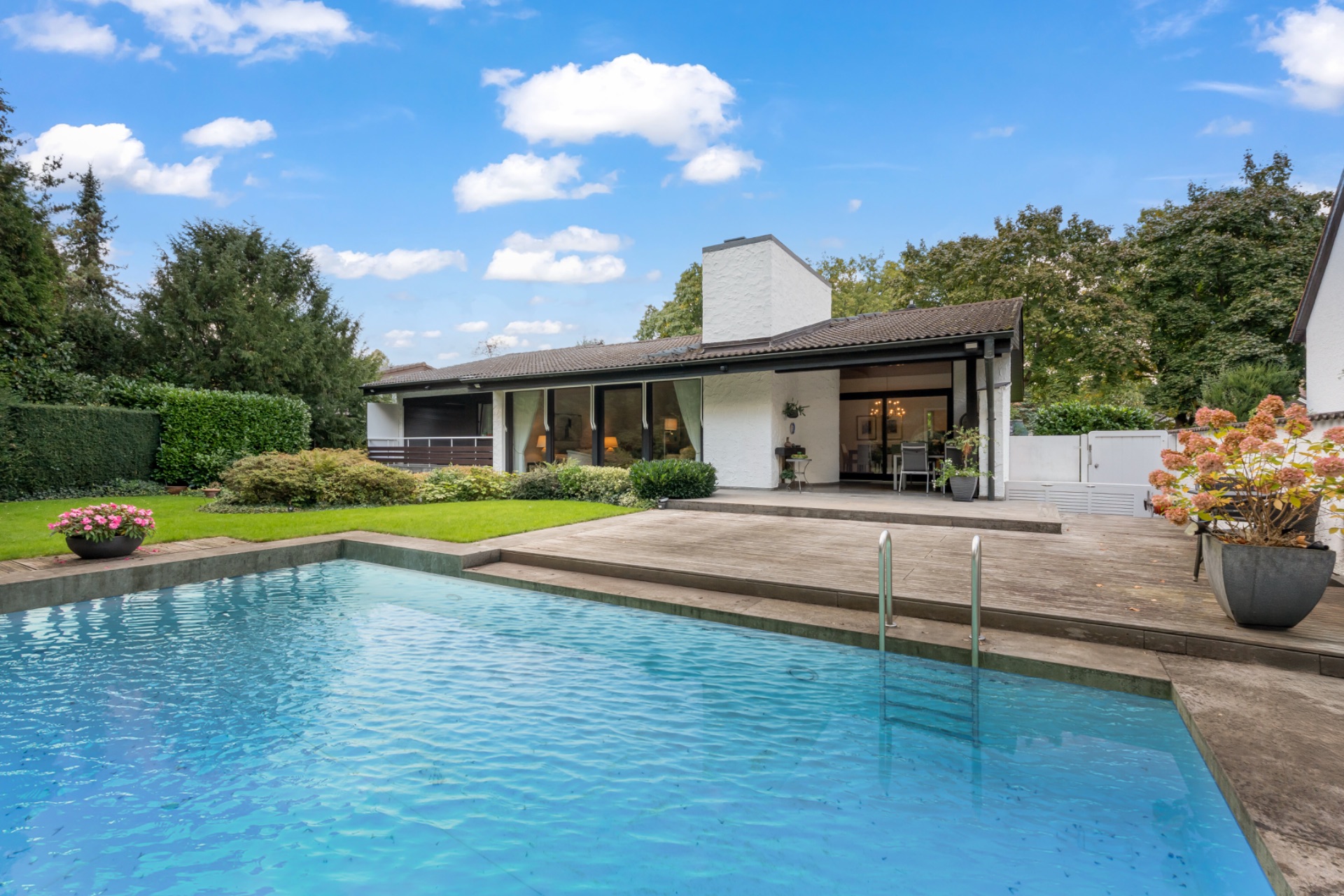 Einfamilienhaus mit großer Terrasse, Garten und Swimmingpool an einem sonnigen Tag.