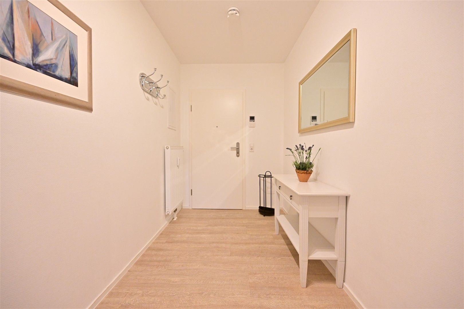 Heller Flur mit Holzboden, weißer Kommode, Spiegel und einem Bild an der Wand.