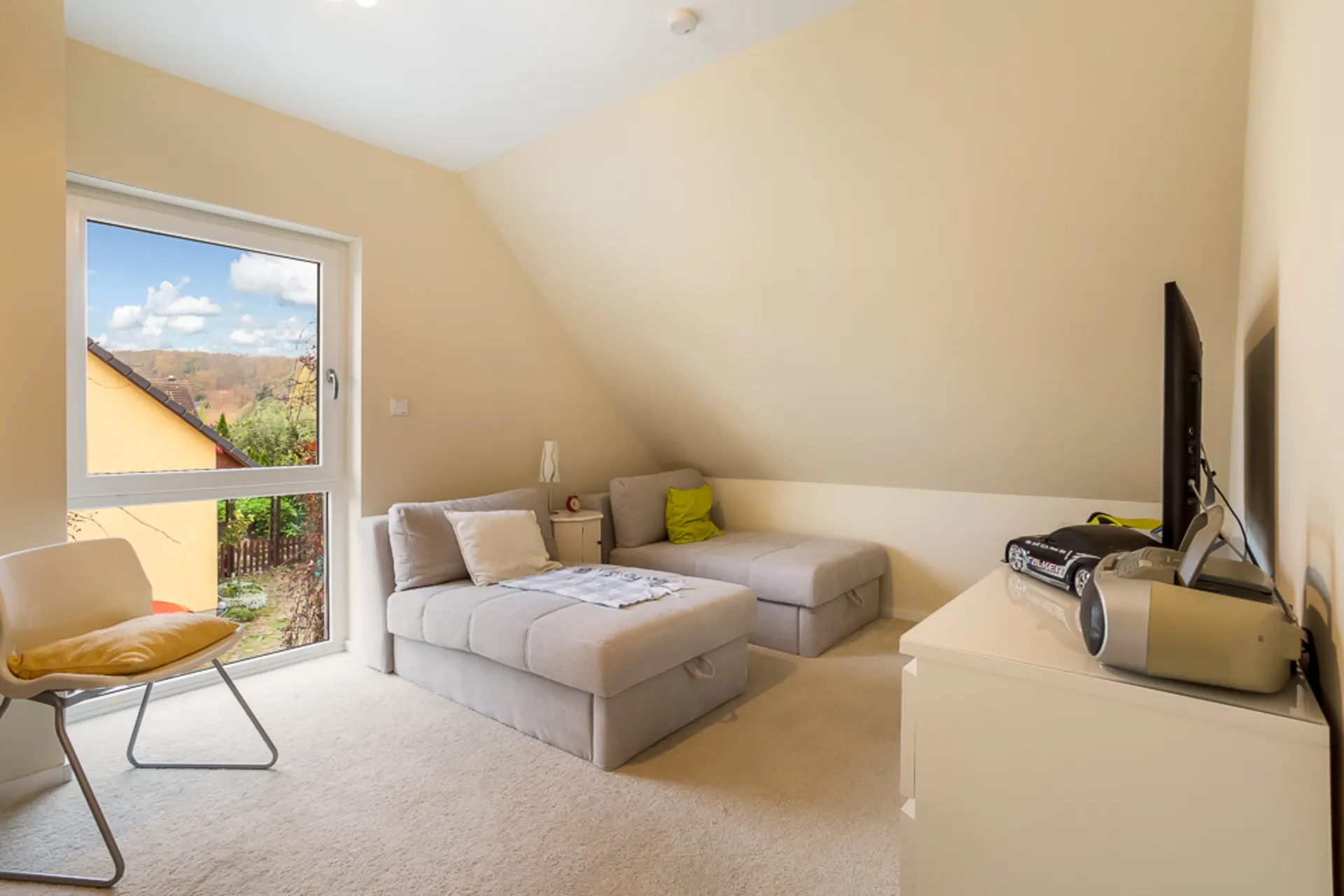 Helles Wohnzimmer mit Sofas, Sessel, großem Fenster und Fernseher auf einer Kommode.