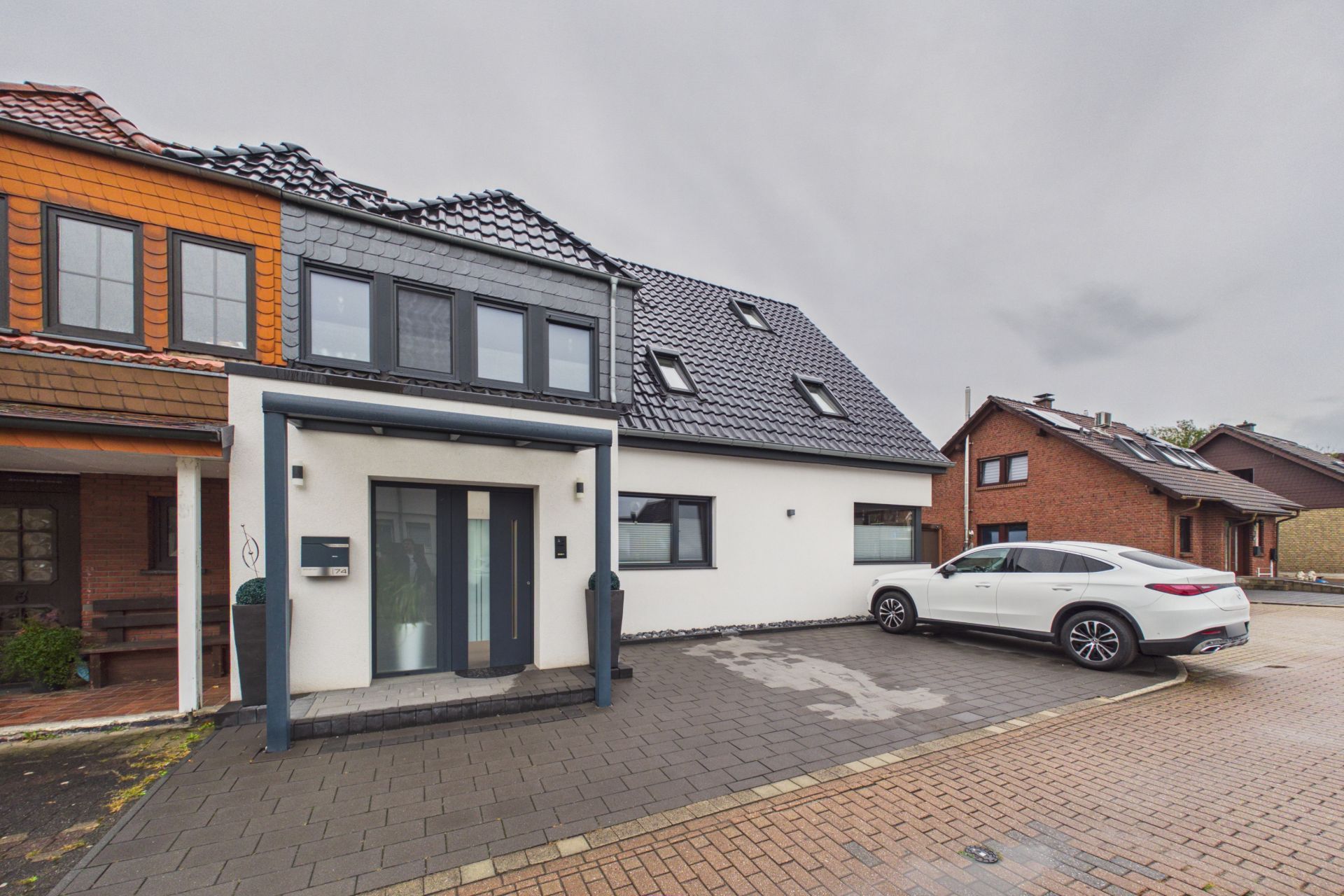 Modernes Wohnhaus mit schwarzem Dach, weißen Wänden und geparktem weißem Auto vor dem Haus.