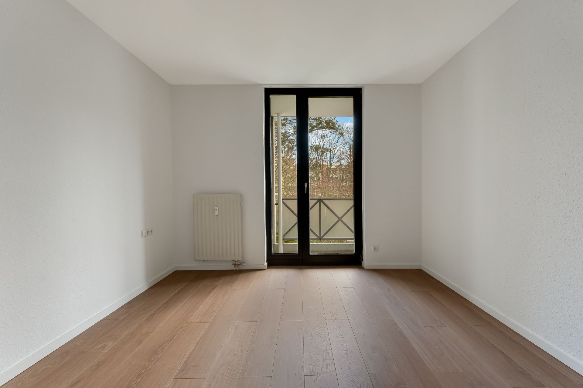 Leerer Raum mit Holzfußboden, weißer Wand und Glastür zu einem Balkon.