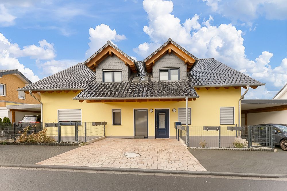 Doppelhaushälfte mit gelber Fassade, zwei Eingängen und Pflastersteinzufahrt.