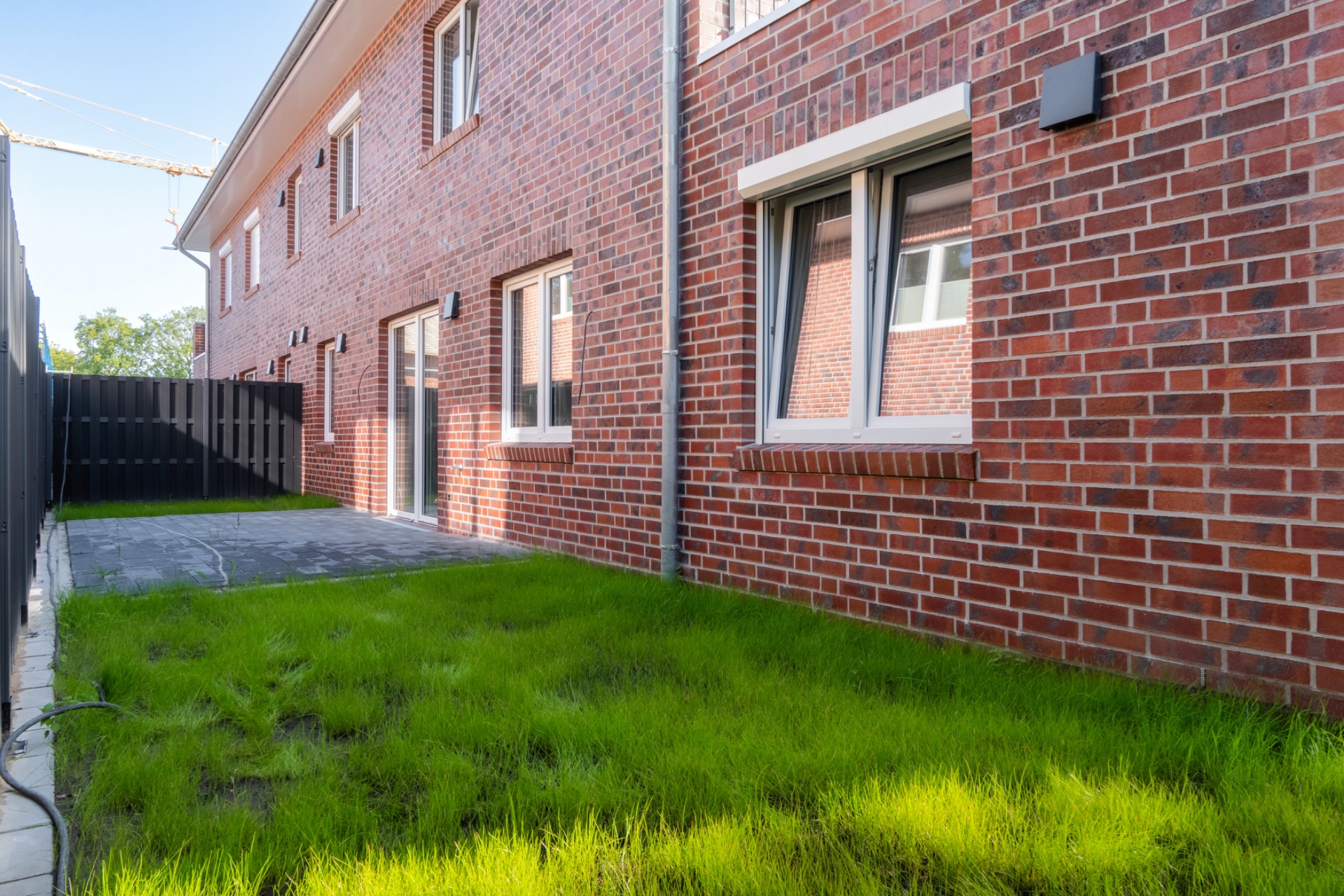 Grüner Rasen und Terrasse neben einem modernen roten Backsteingebäude mit Fenstern.