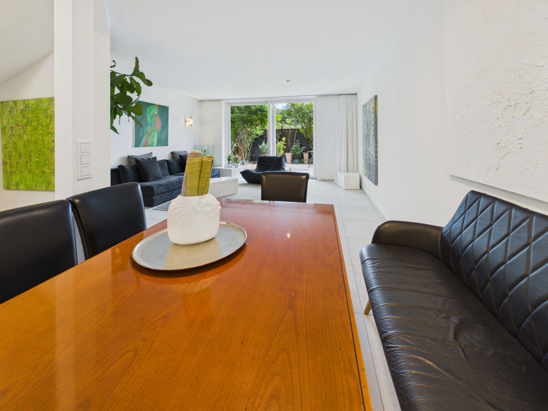 Modernes Wohnzimmer mit großem Holztisch, Ledersofa und Blick auf Garten durch Glas-Schiebetüren.