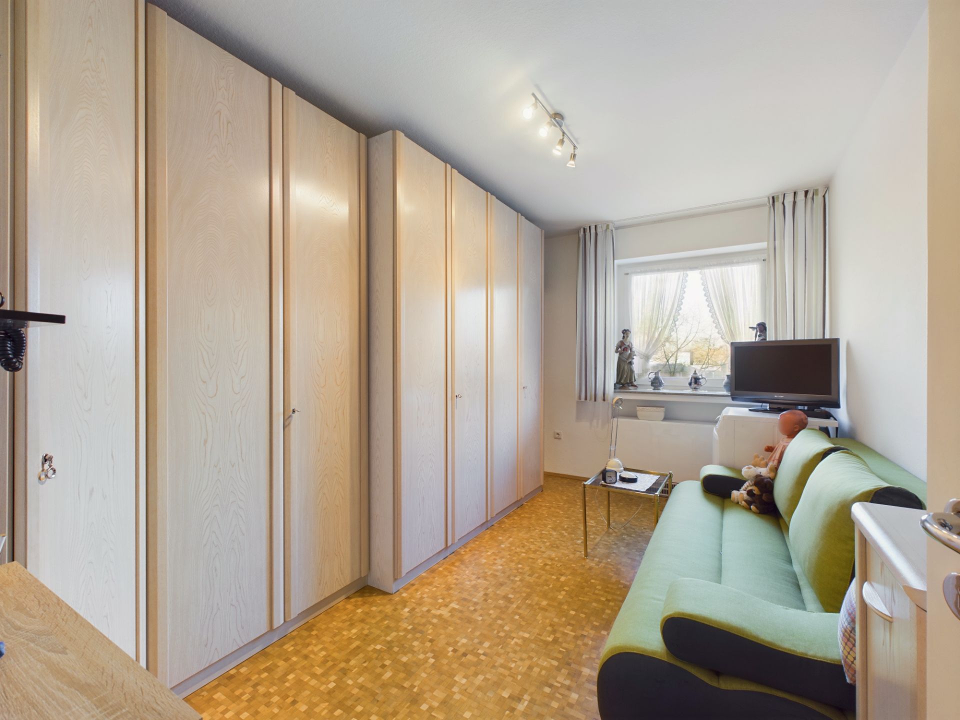 Zimmer mit großen Einbauschränken, grünem Sofa, kleinem Tisch und Fenster mit Fernseher.