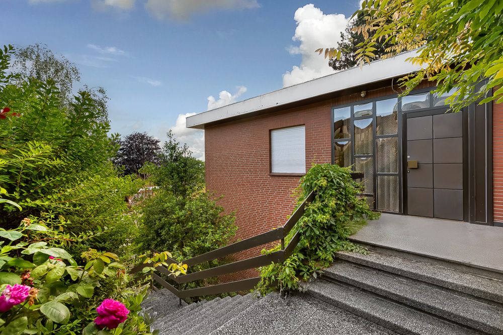 Außentreppe mit Pflanzen führt zum Eingang eines Backsteinhauses.