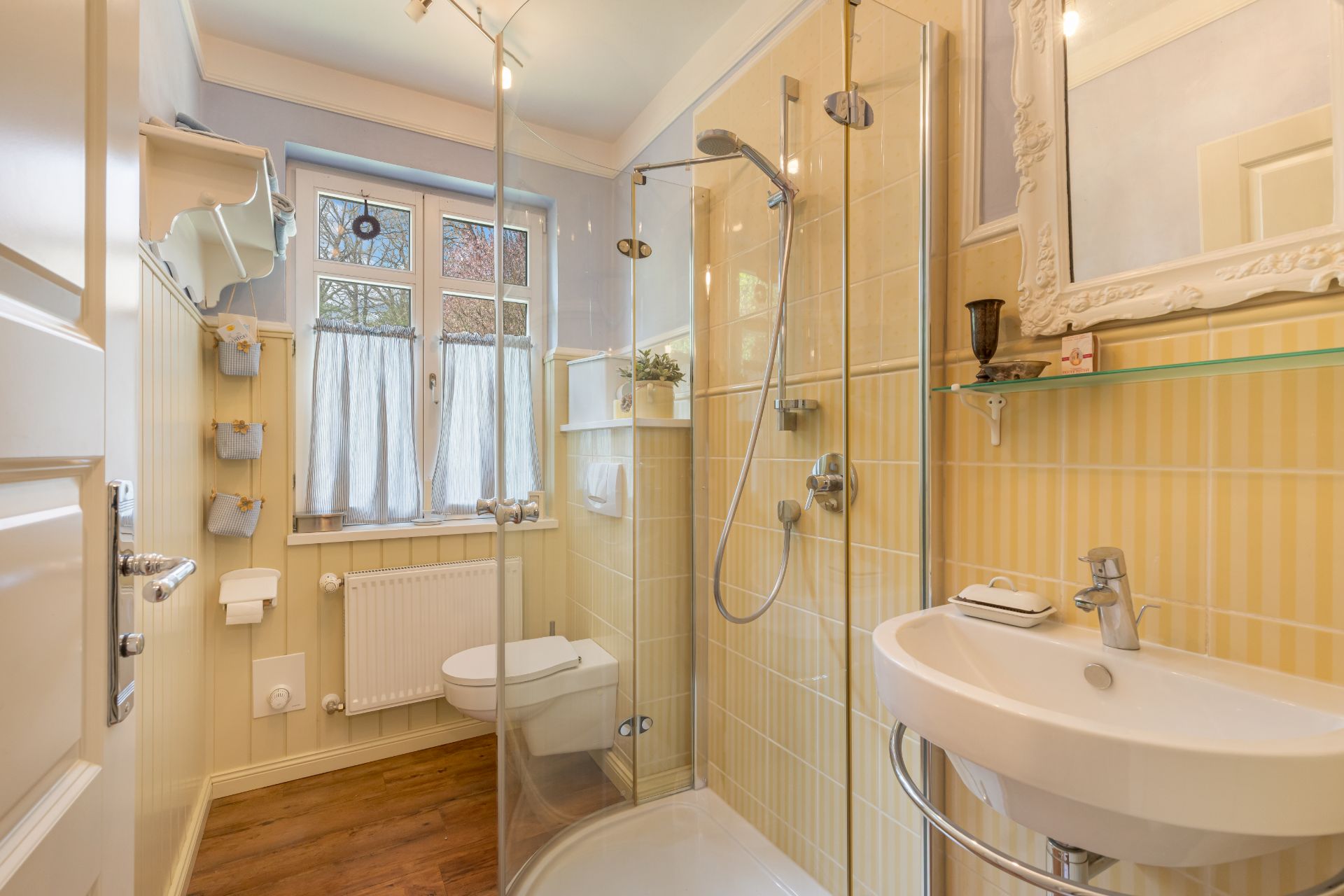 Kleines Badezimmer mit Dusche, WC, Waschbecken und Fenster mit Vorhängen.