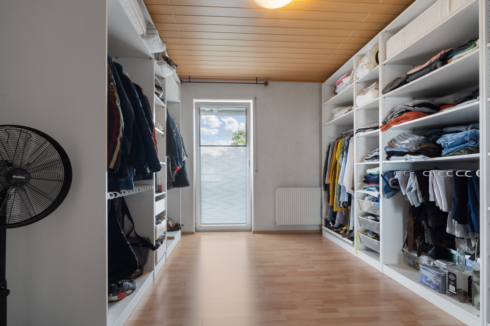 Großer begehbarer Kleiderschrank mit Regalen, Hängekleidung, gefaltetem Textil und einem Standventilator.