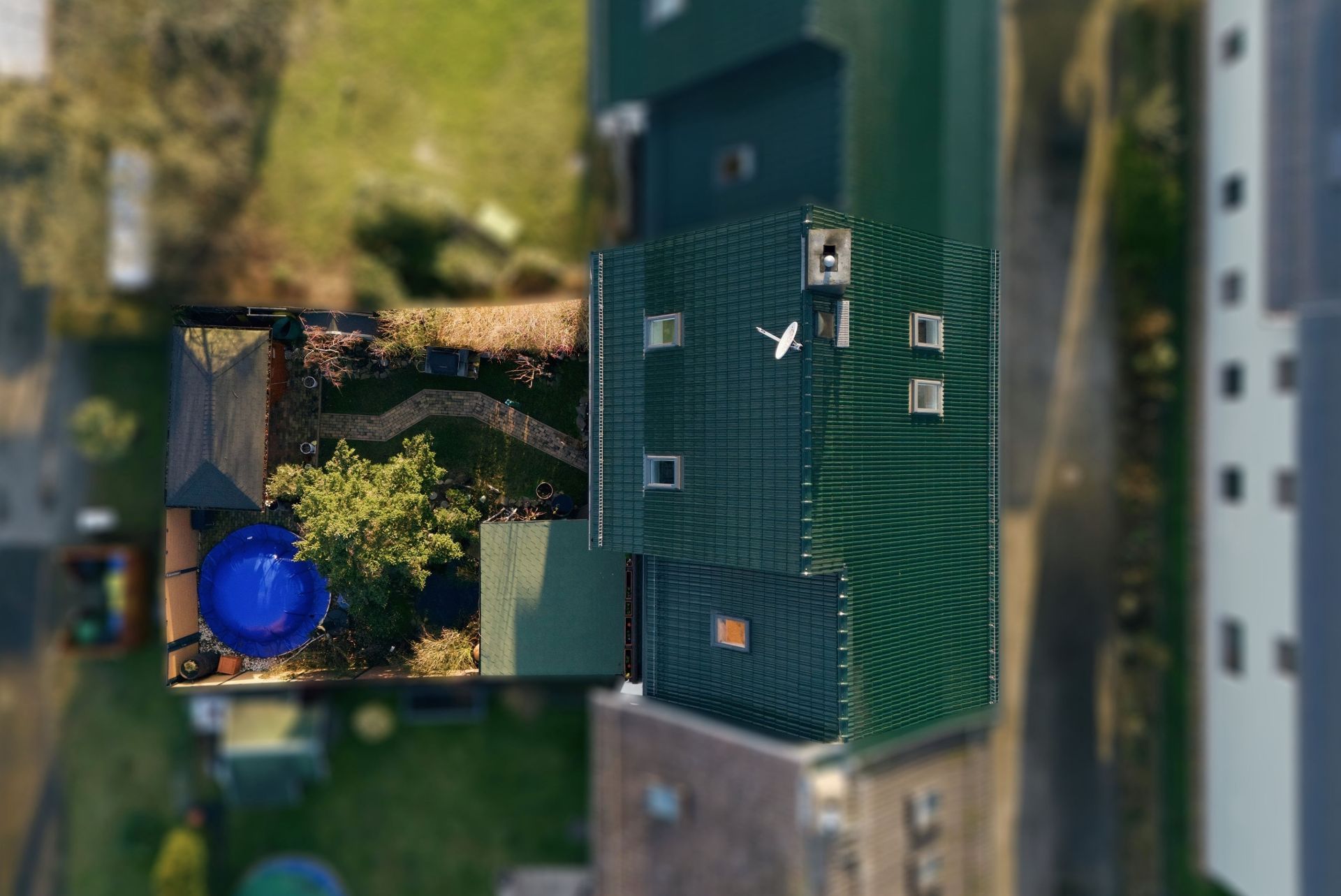Luftaufnahme eines Hauses mit grünem Dach und Garten mit blauem Trampolin.