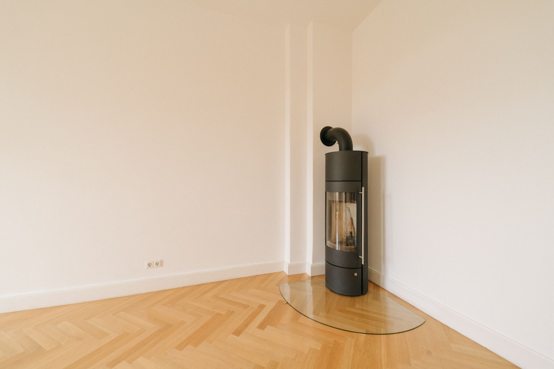 Leerer Raum mit Holzfußboden und modernem schwarzen Kamin in der Ecke.