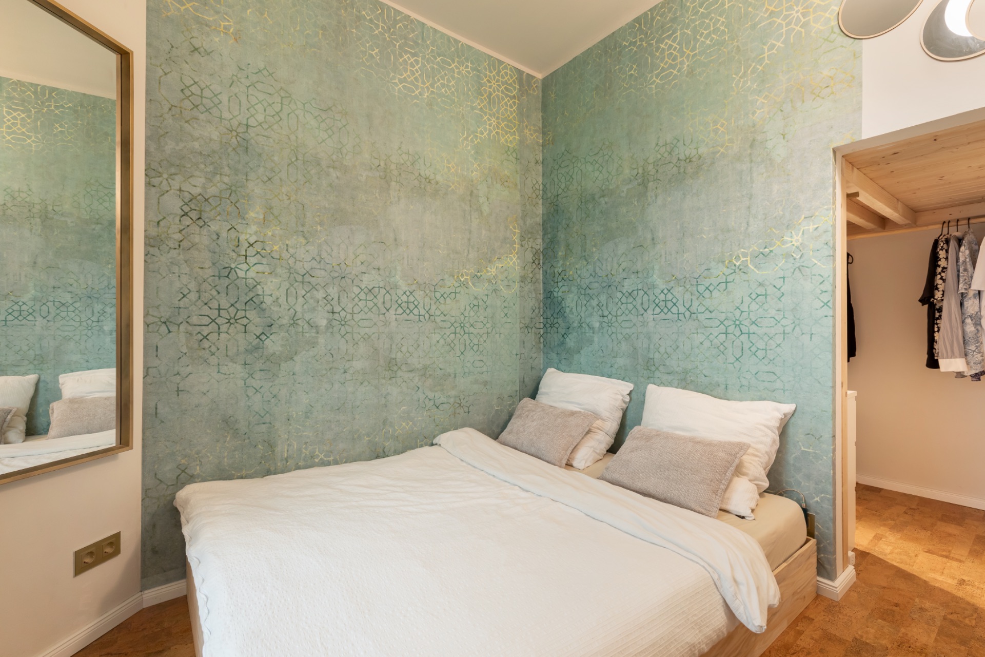 Schlafzimmer mit Doppelbett, türkisfarbener Wand und offenem Kleiderschrank.