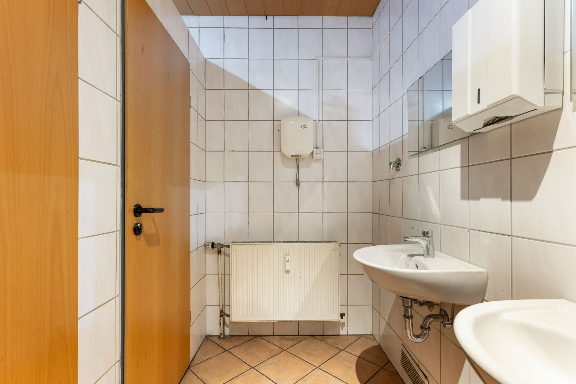 Kleines Badezimmer mit Waschbecken, Spiegel, Heizung und gefliesten Wänden.