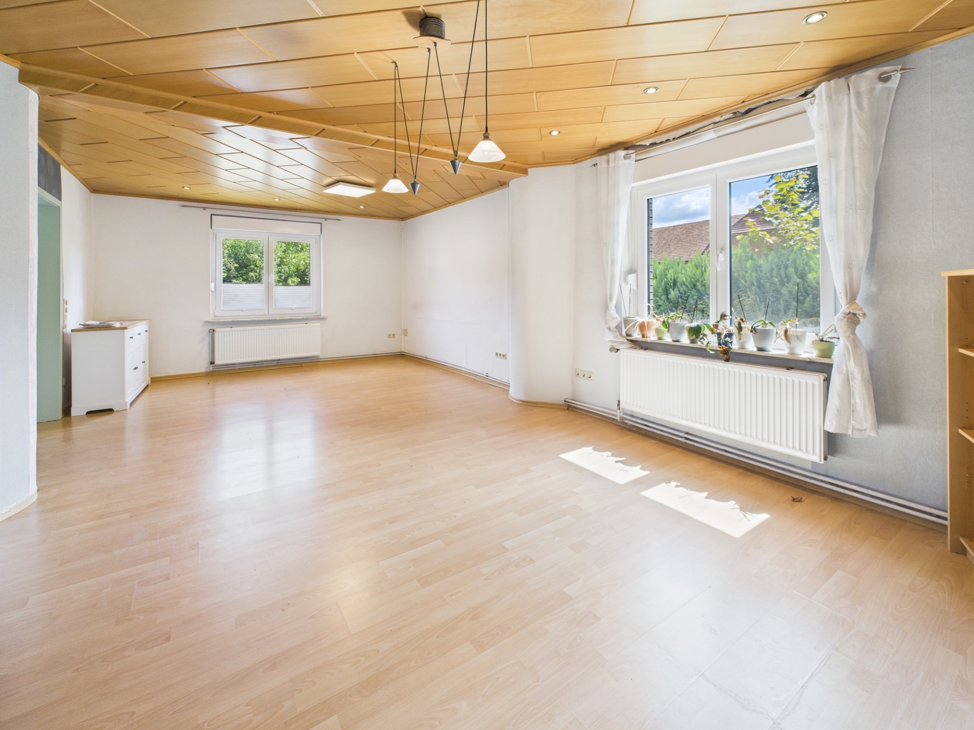 Helles, leeres Wohnzimmer mit Holzdecke, großen Fenstern und Holzfußboden.