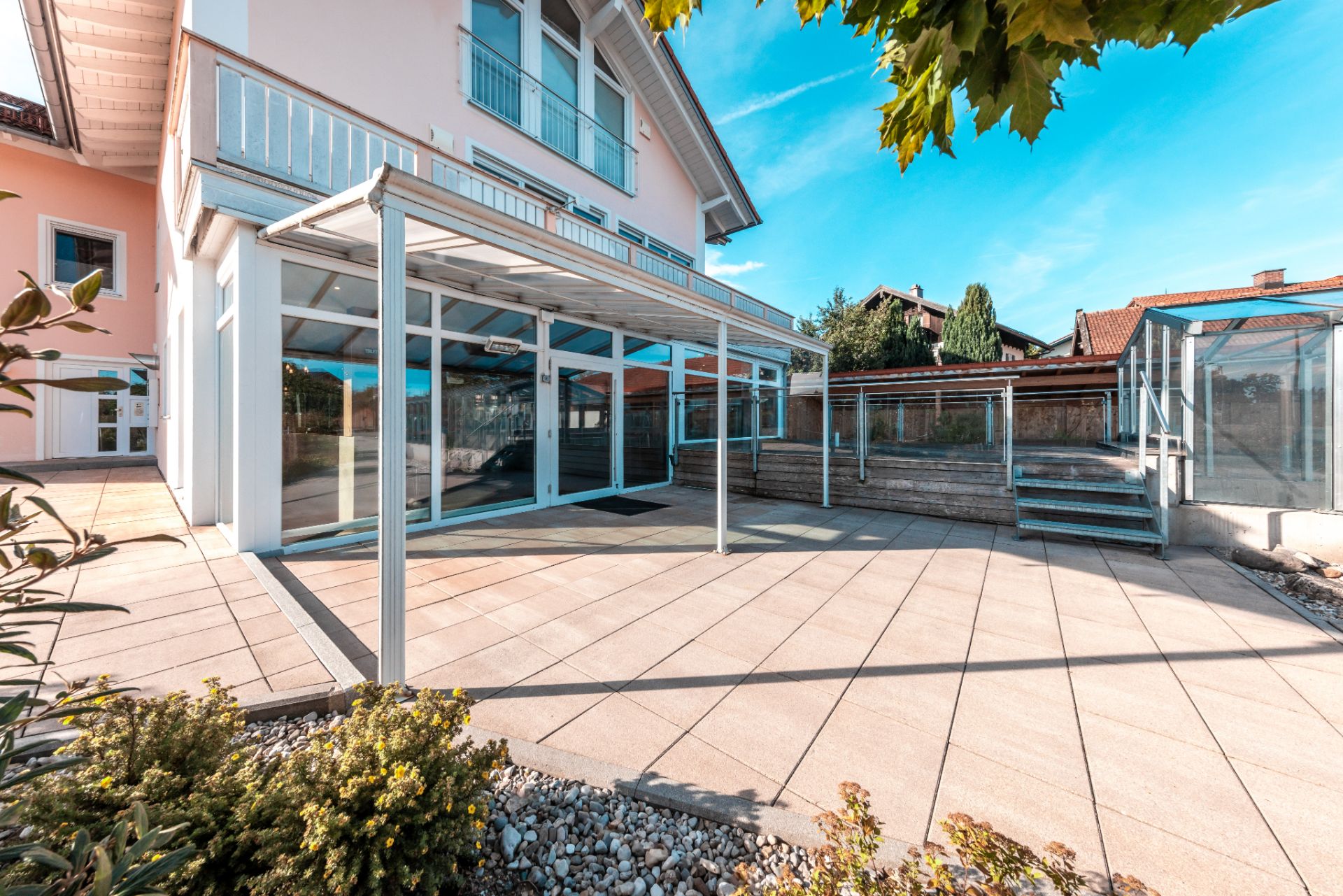 Große Terrasse mit Glasüberdachung an einem Wohnhaus, Treppe und Pflanzen sichtbar.