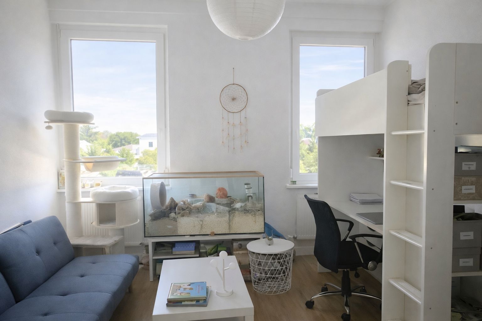 Helles Zimmer mit Hochbett, Schreibtisch, Sofa, Aquarium und zwei großen Fenstern.