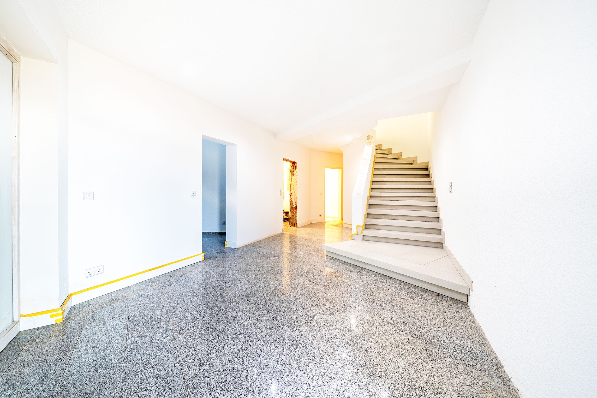Heller Flur mit Treppe, glänzendem Boden und weißen Wänden in einem Wohnhaus.