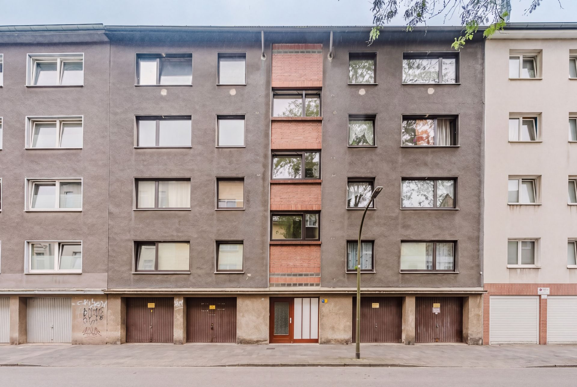 Wohnhaus mit vier Etagen, mehreren Fenstern und Garagentoren im Erdgeschoss.