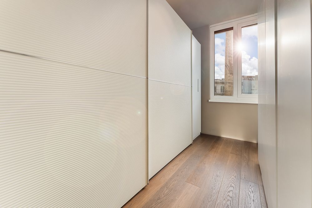 Schmaler Raum mit Einbauschrank, Holzfußboden und Fenster, durch das Sonnenlicht scheint.