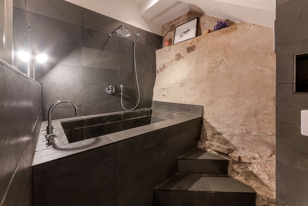 Modernes Bad mit dunkler Fliesenwanne, Dusche und rustikaler Steinwand.