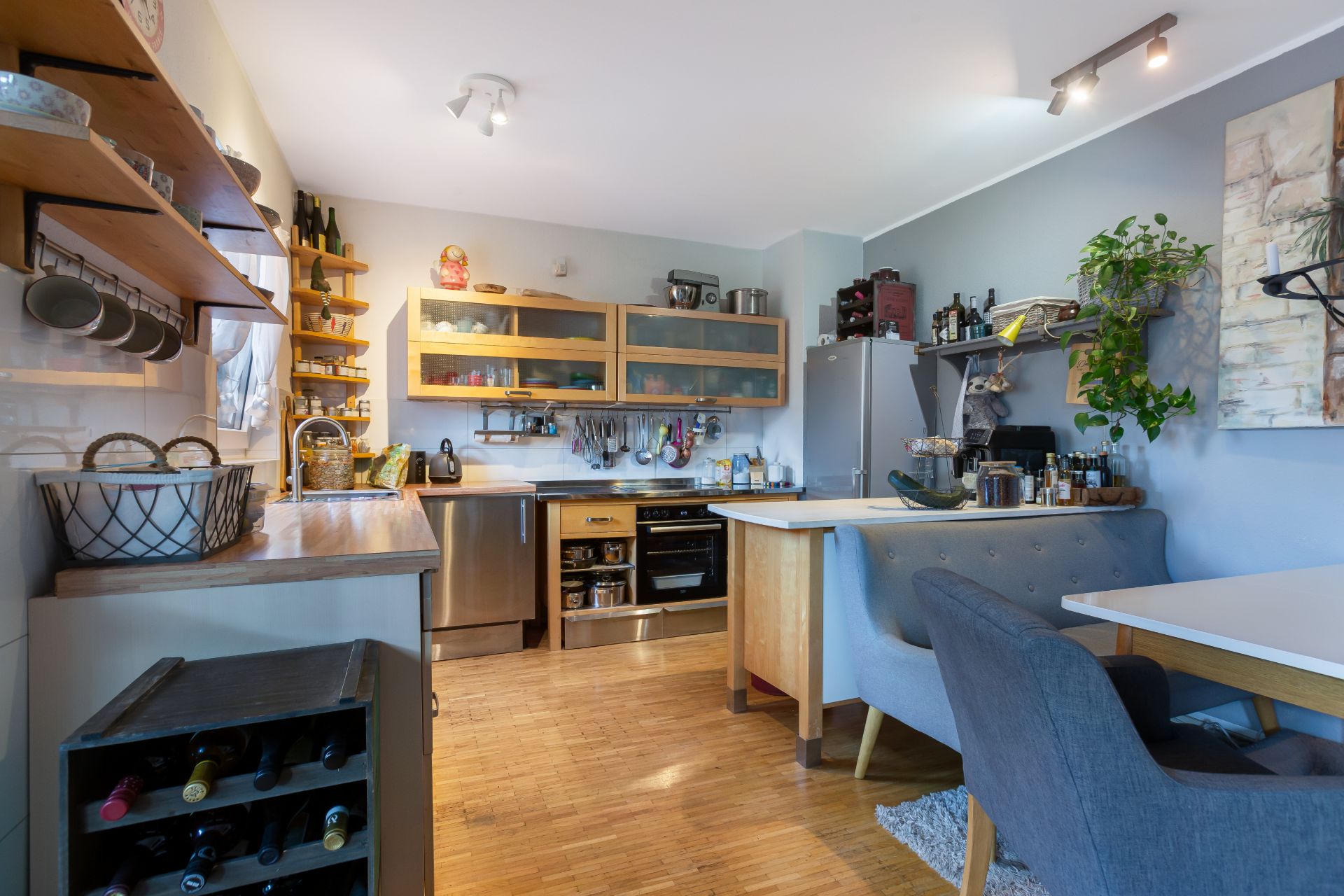 Moderne Küche mit Holzregalen, Geräten, Esstisch und grauen Stühlen auf Holzboden.